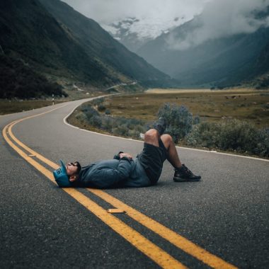 man lying on black concrete top road near green leafed plants