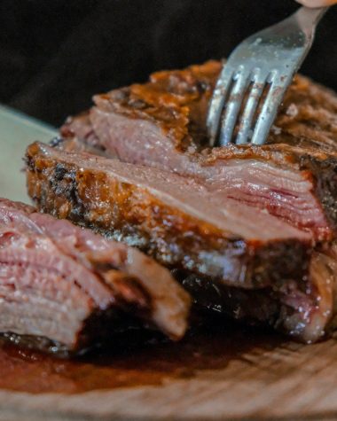 person slicing a meat on brown wooden board