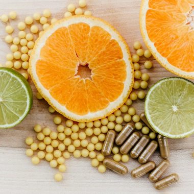 Citrus slices, small yellow supplement beads, and brown capsules on a wooden surface